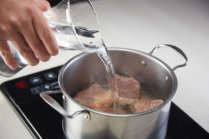agregando agua a carne cocinando en una olla 
